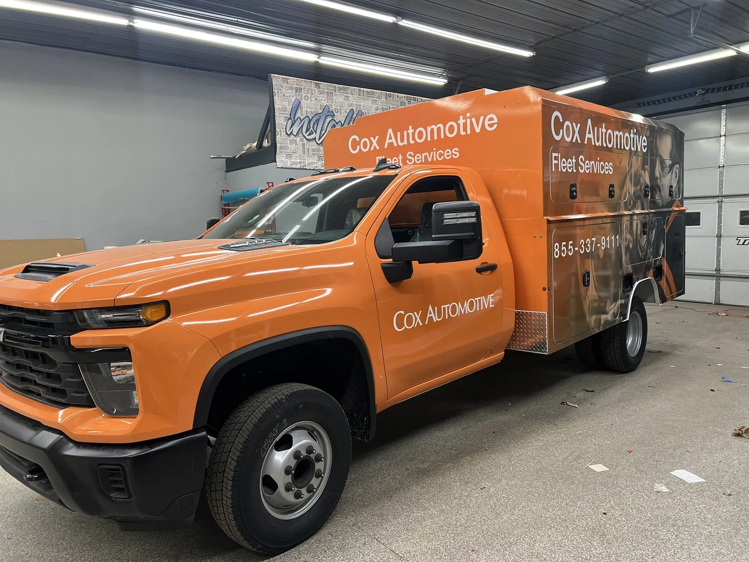 An orange Cox Automotive service truck with custom commercial wrap graphics
